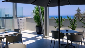 A rooftop terrace with outdoor seating, a large umbrella, and a view of the sea. - Mercure Larnaca Finikoudes Beach (Larnaca)