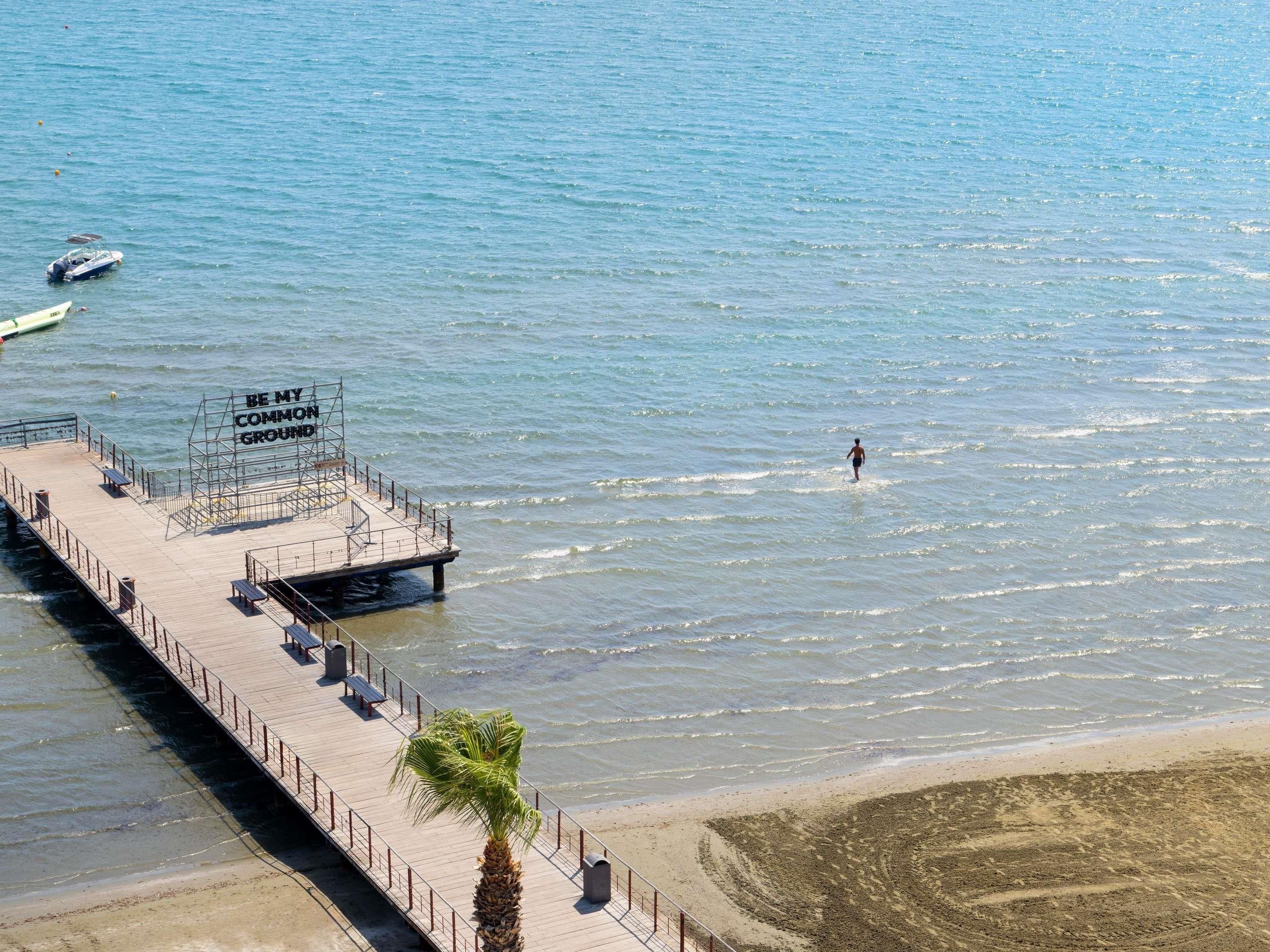 Un muelle se adentra en aguas tranquilas, con una persona caminando por la playa.