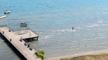 Un muelle se adentra en aguas tranquilas, con una persona caminando por la playa.