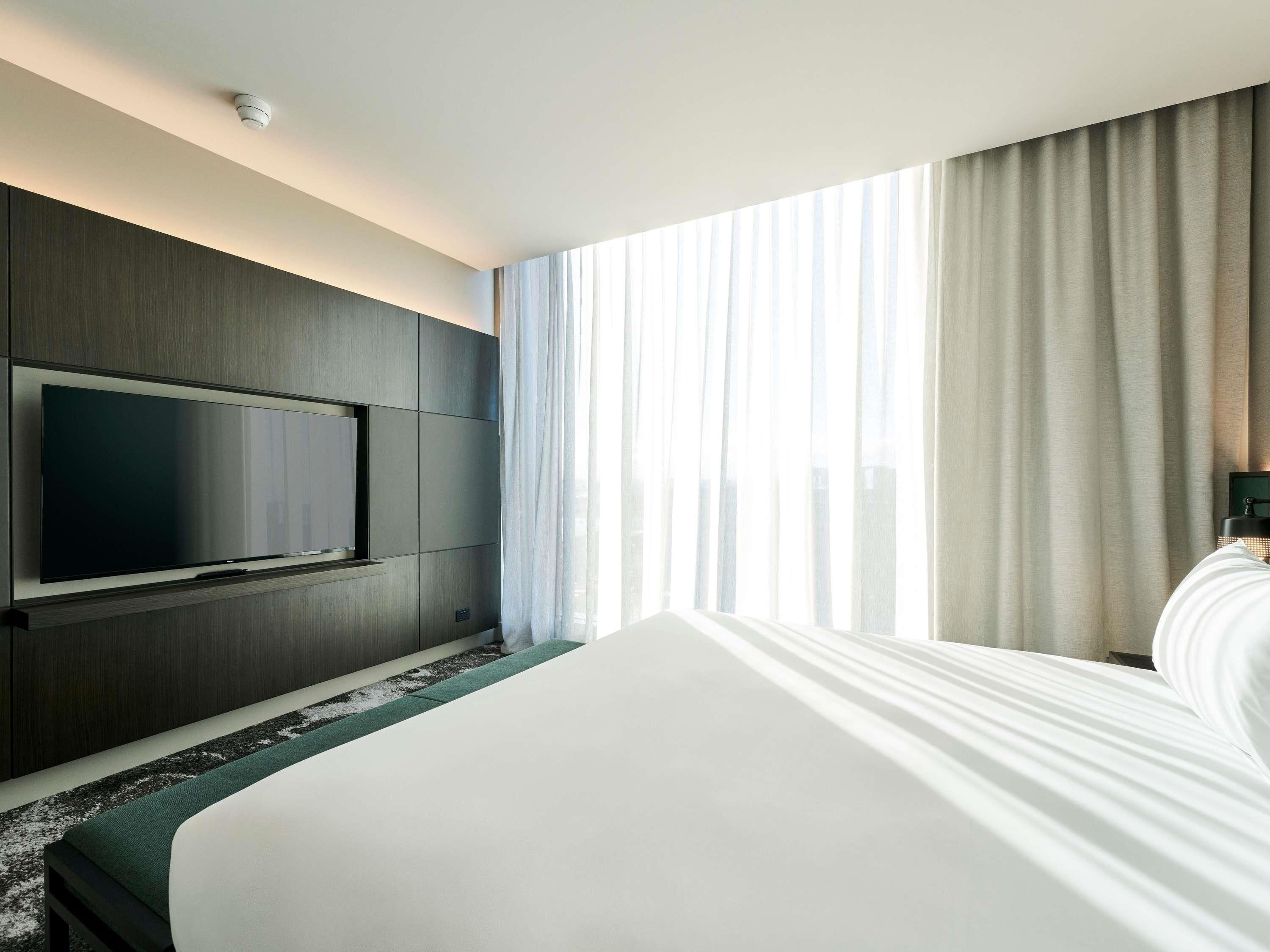 Habitación de hotel con una cama grande, un televisor de pantalla plana en la pared y una ventana con cortinas.