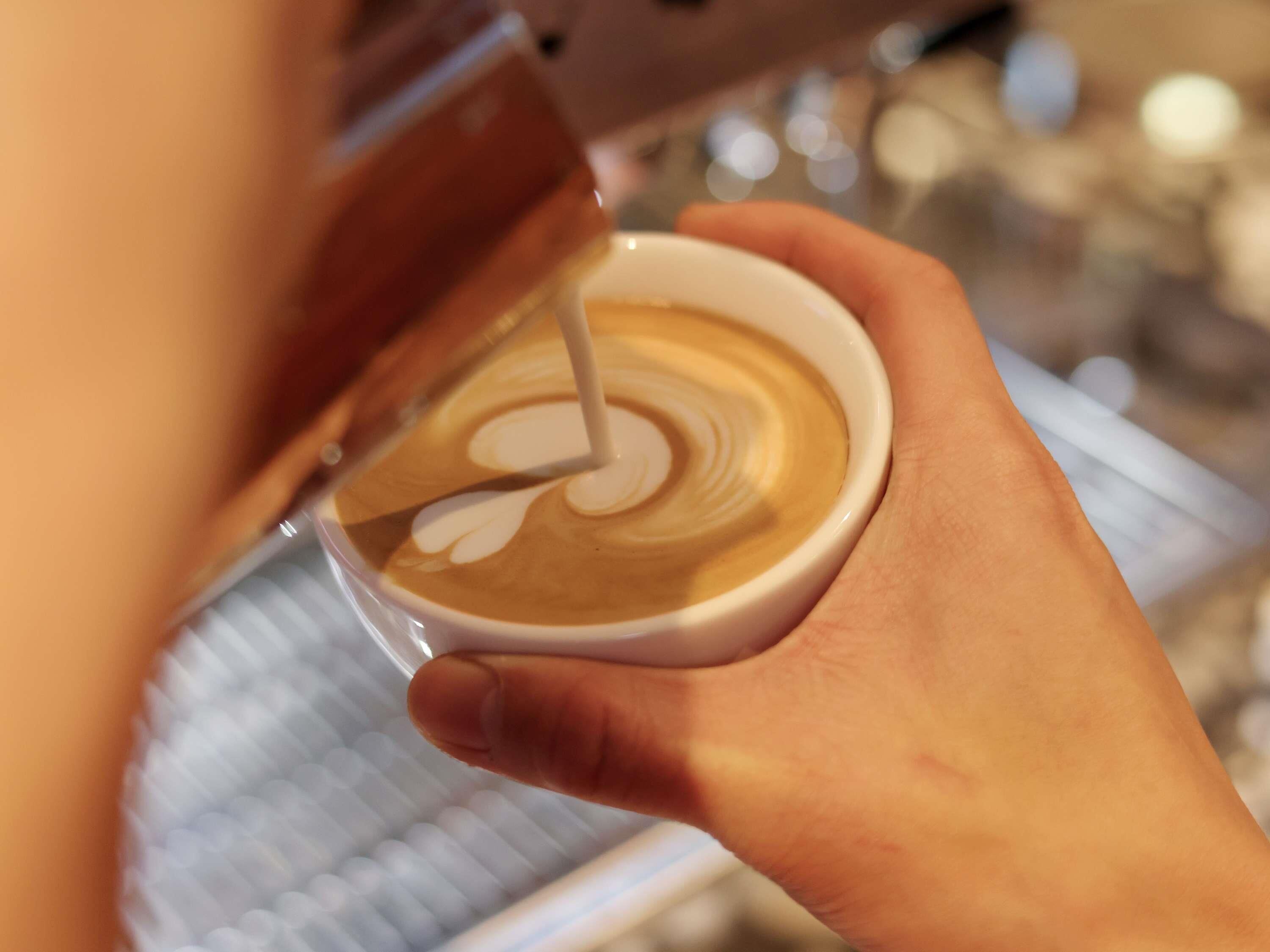 A person holding a cup of coffee with a latte art design.