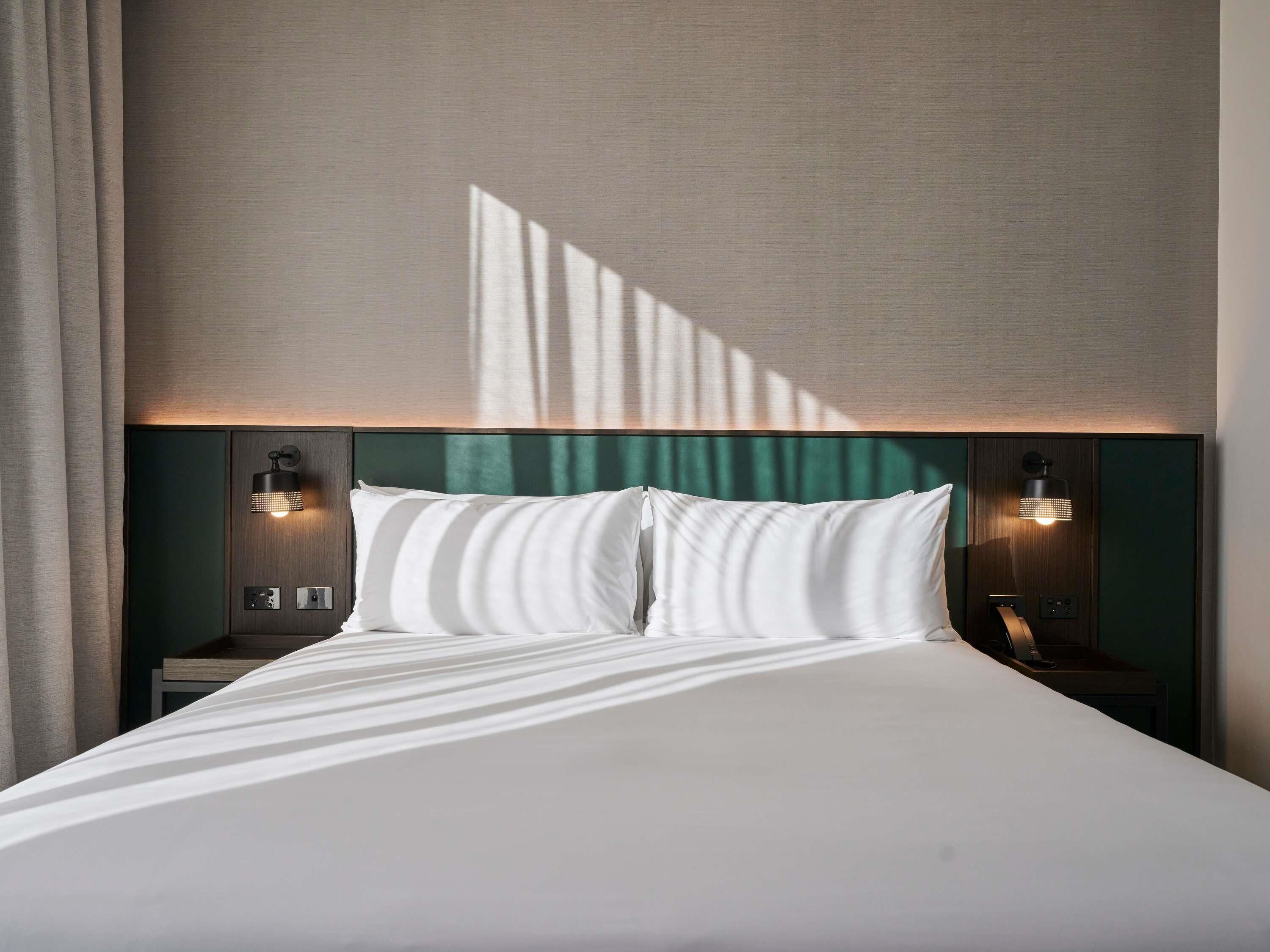 Una habitación de hotel con una cama grande, dos mesitas de noche y lámparas de pared.