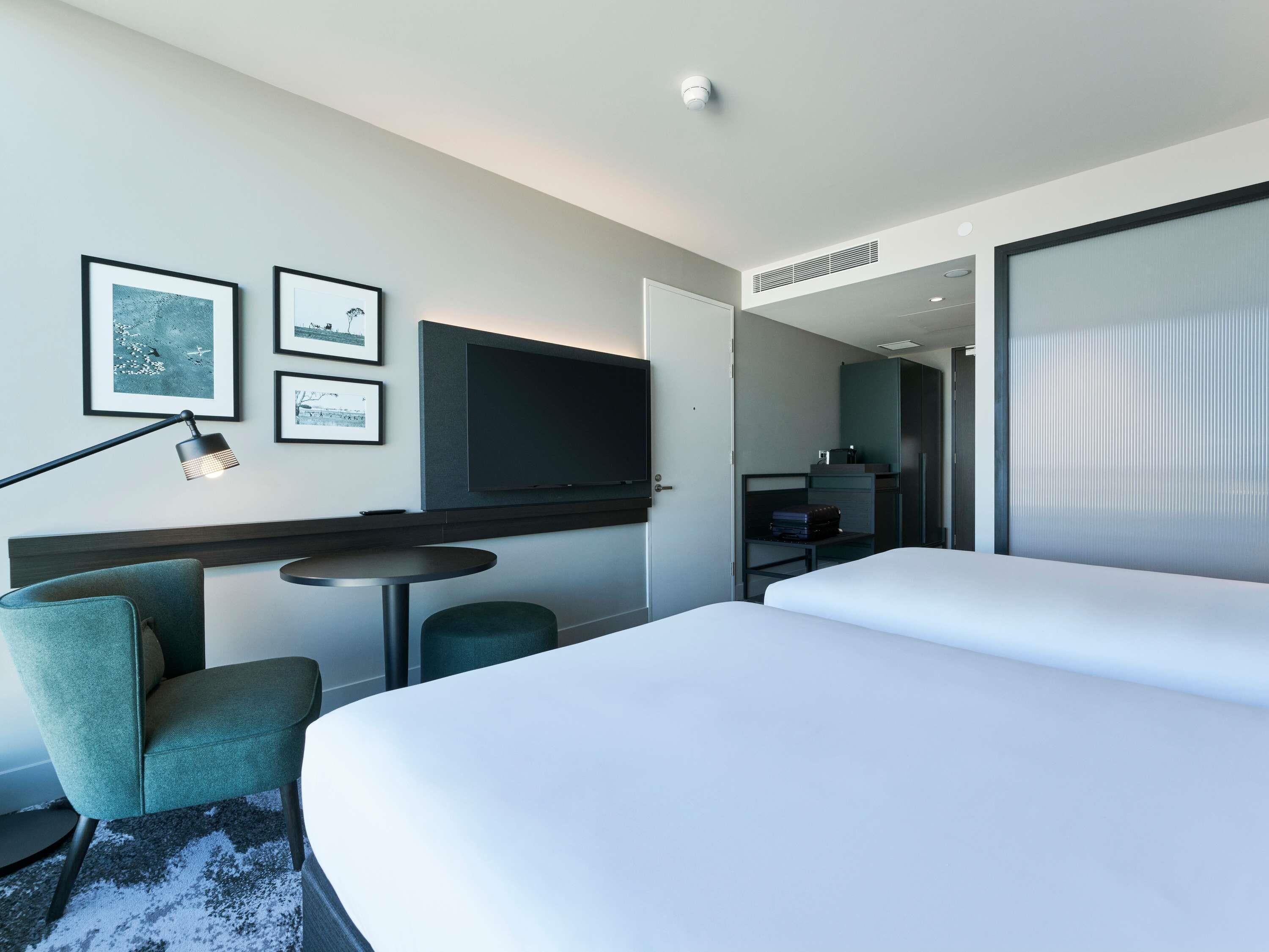 Een moderne hotelkamer met een bed, een bureau, een stoel, een televisie en lijstjes met foto's aan de muur.
