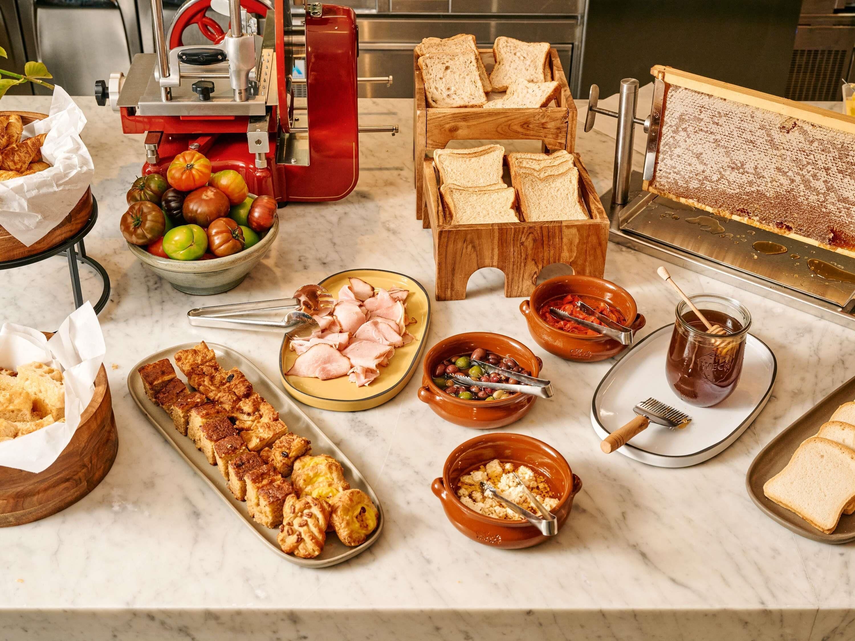 A breakfast buffet with various food items, including bread, ham, pastries, and condiments.
