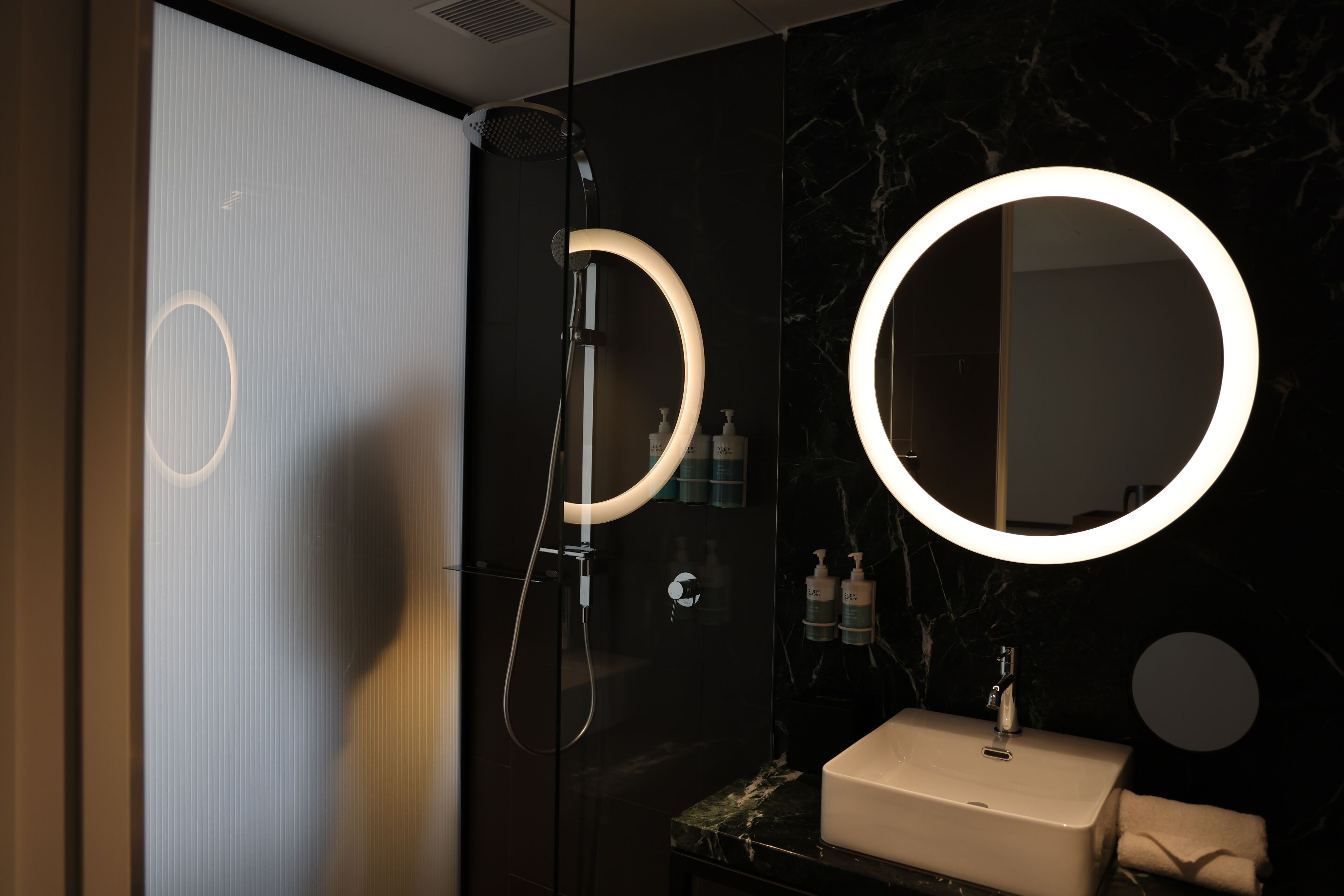 A modern bathroom with a glass-enclosed shower, a vanity with a marble countertop, and two illuminated mirrors.