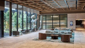 A spacious lobby with a modern design, featuring a seating area with sofas and armchairs, a large glass wall offering a view of greenery, and a ceiling with a geometric pattern. - Novotel Melbourne Airport (Melbourne Airport)