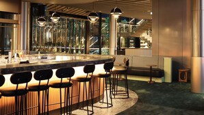 A modern bar area with a curved counter, bar stools, and pendant lighting. - Novotel Melbourne Airport (Melbourne Airport)