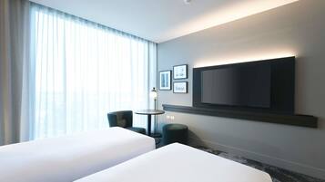 Habitación de hotel con dos camas, un televisor de pantalla plana montado en la pared, una mesita y una silla.