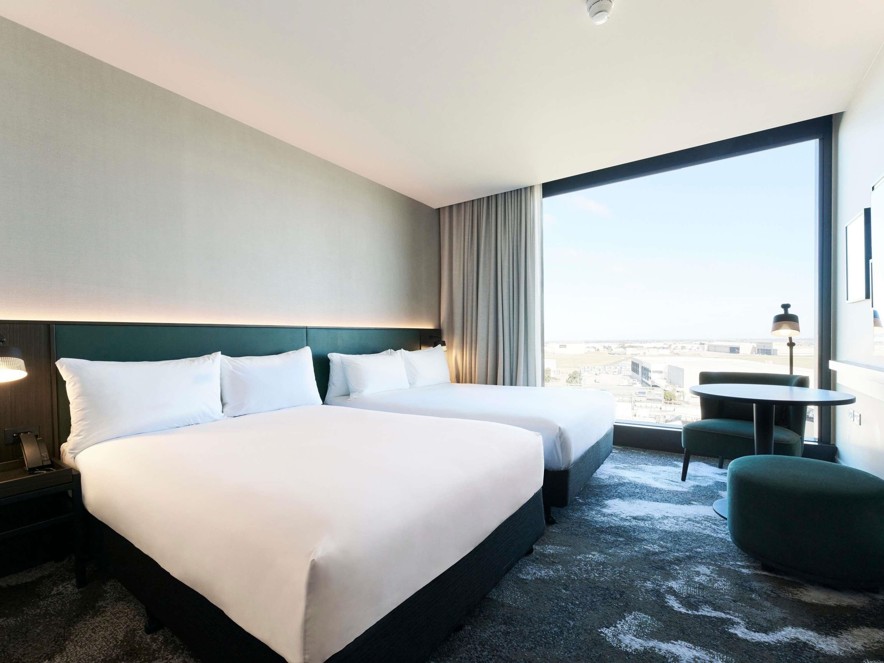Habitación de hotel con dos camas, vistas a la ciudad, una mesita y una silla.