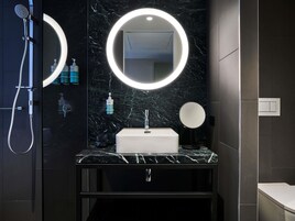 Un baño moderno con encimera de mármol, lavabo empotrado, cabezal de ducha de mano y dos espejos fijos en la pared con iluminación integrada.