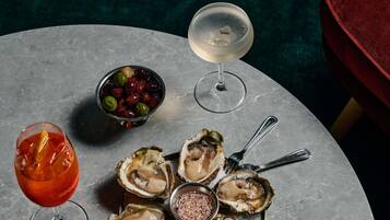 A table with oysters, a bowl of olives, and two glasses of drink.