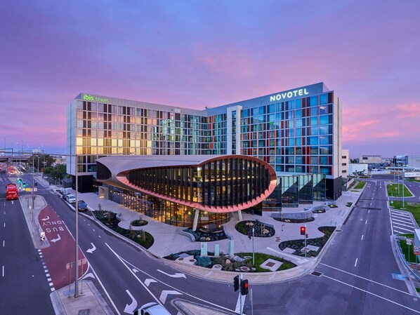 A modern hotel with a curved glass facade, a prominent 'NOVOTEL' sign, and a well-maintained urban setting.