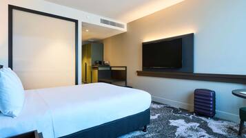 A hotel room with a bed, a TV mounted on the wall, a desk with a chair, and a suitcase on the floor.