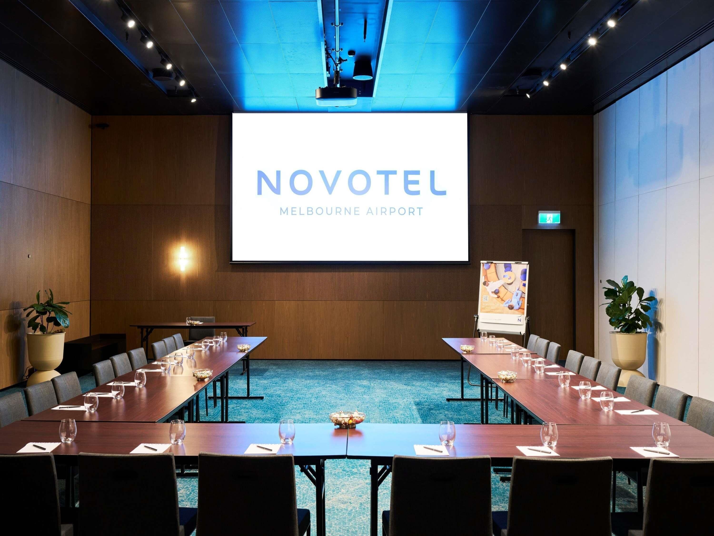 A conference room with a large screen displaying 'NOVOTEL MELBOURNE AIRPORT'.