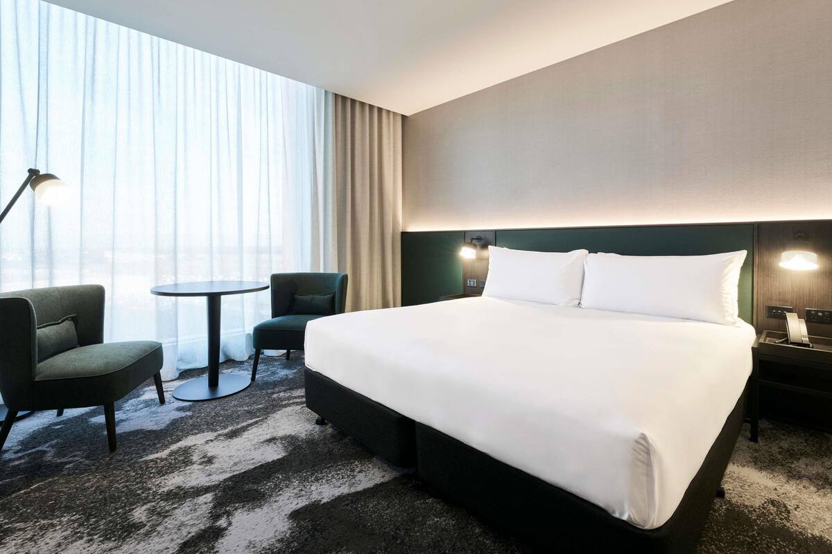 A hotel room with a large bed, two chairs, a small table, and a lamp.