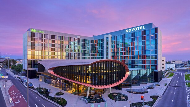 A modern hotel with a curved glass facade, a prominent 'Novotel' sign, and a 'ibis Styles' sign. - Novotel Melbourne Airport (Melbourne Airport)