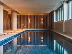 Una piscina interior moderna con suelo de baldosas, pared de listones de madera y barandilla de metal.