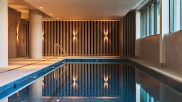 A modern indoor swimming pool with a tiled floor, a wooden slatted wall, and a metal handrail.