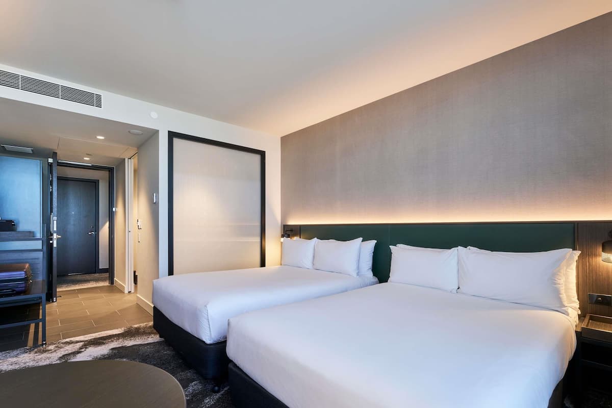 A hotel room with two beds, a desk, and a large window.
