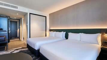 A hotel room with two beds, a desk, and a large window.