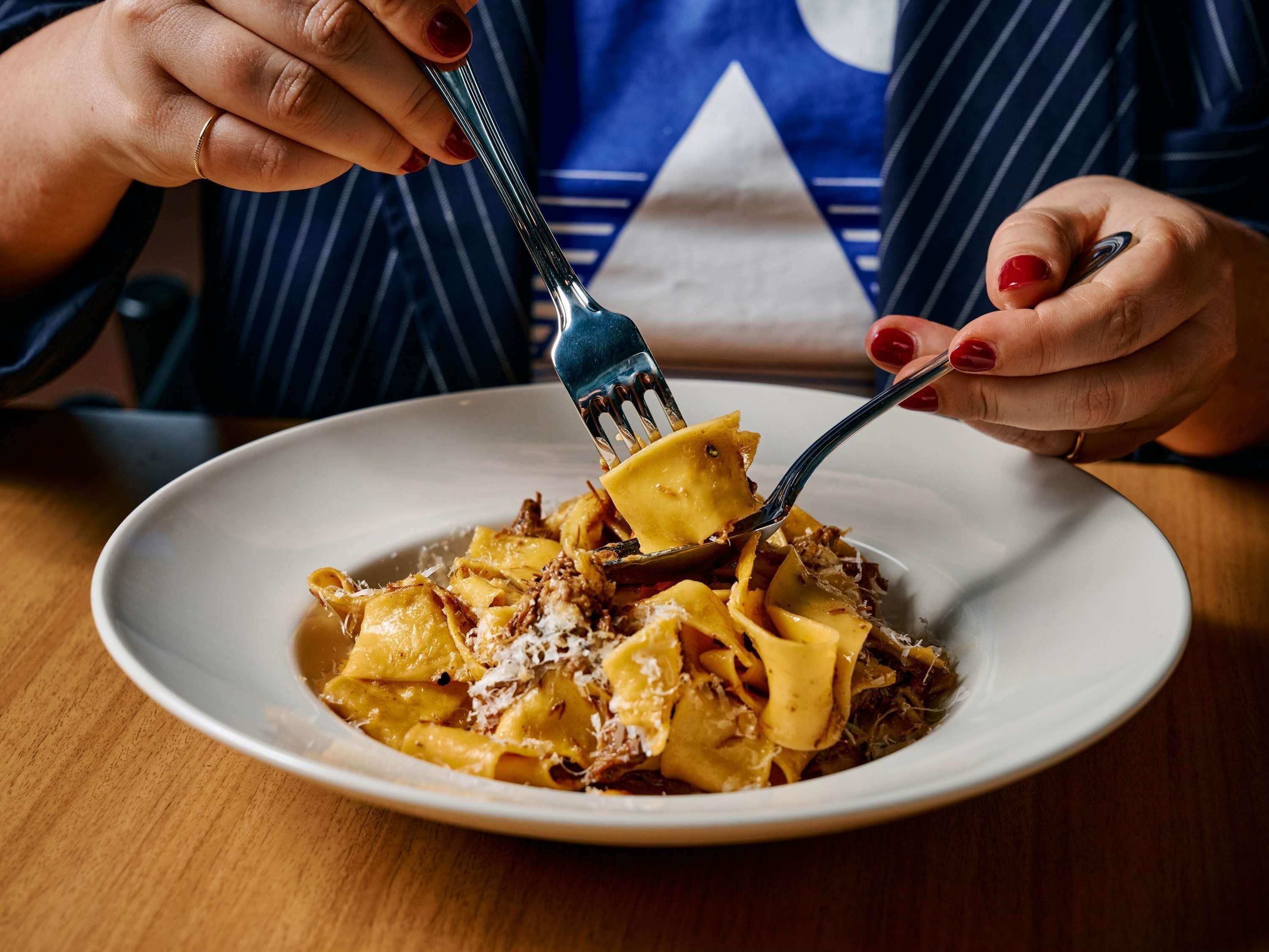 A person holding a fork over a plate of pasta with a fork tine visible.