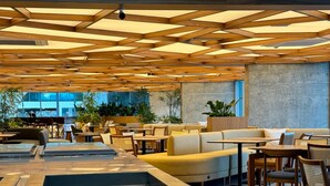 Un espacio interior moderno con paneles de techo de madera, zonas de estar y un gran ventanal que proporciona luz natural.