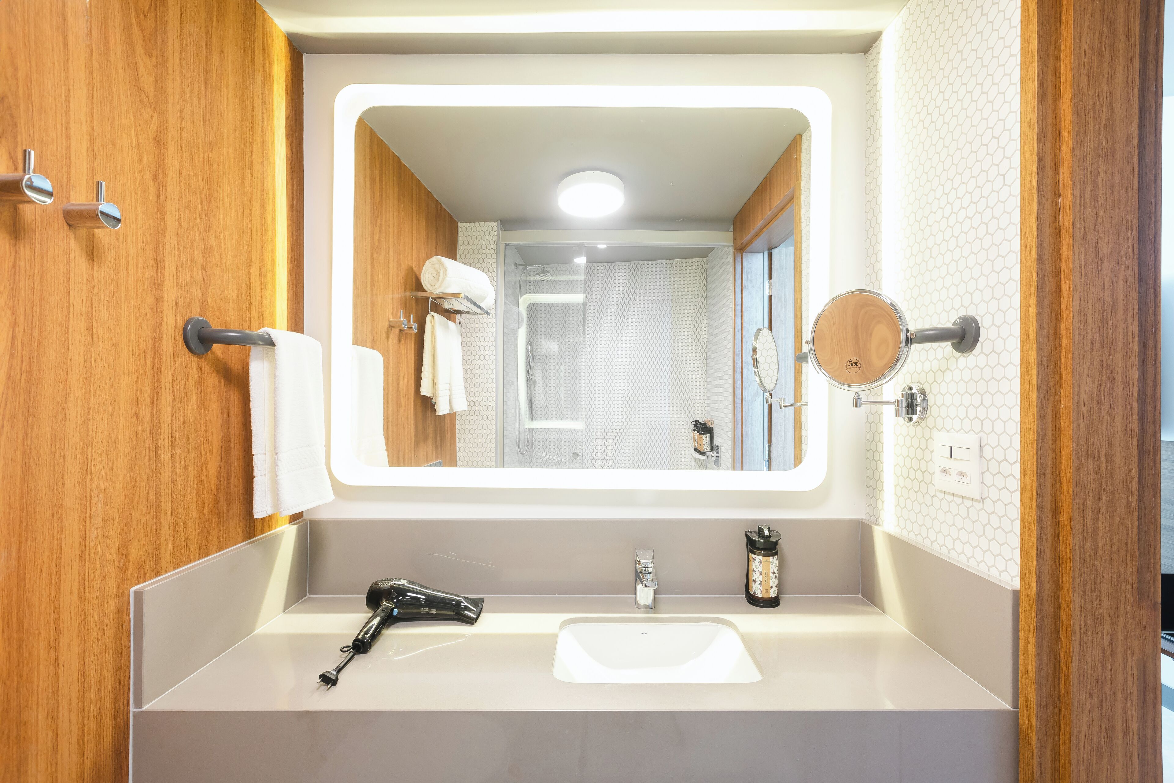 Un baño con un espejo grande, muebles de madera, un lavabo y una zona de ducha.