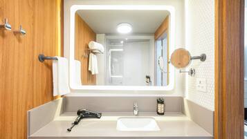 Un baño con un espejo grande, muebles de madera, un lavabo y una zona de ducha.
