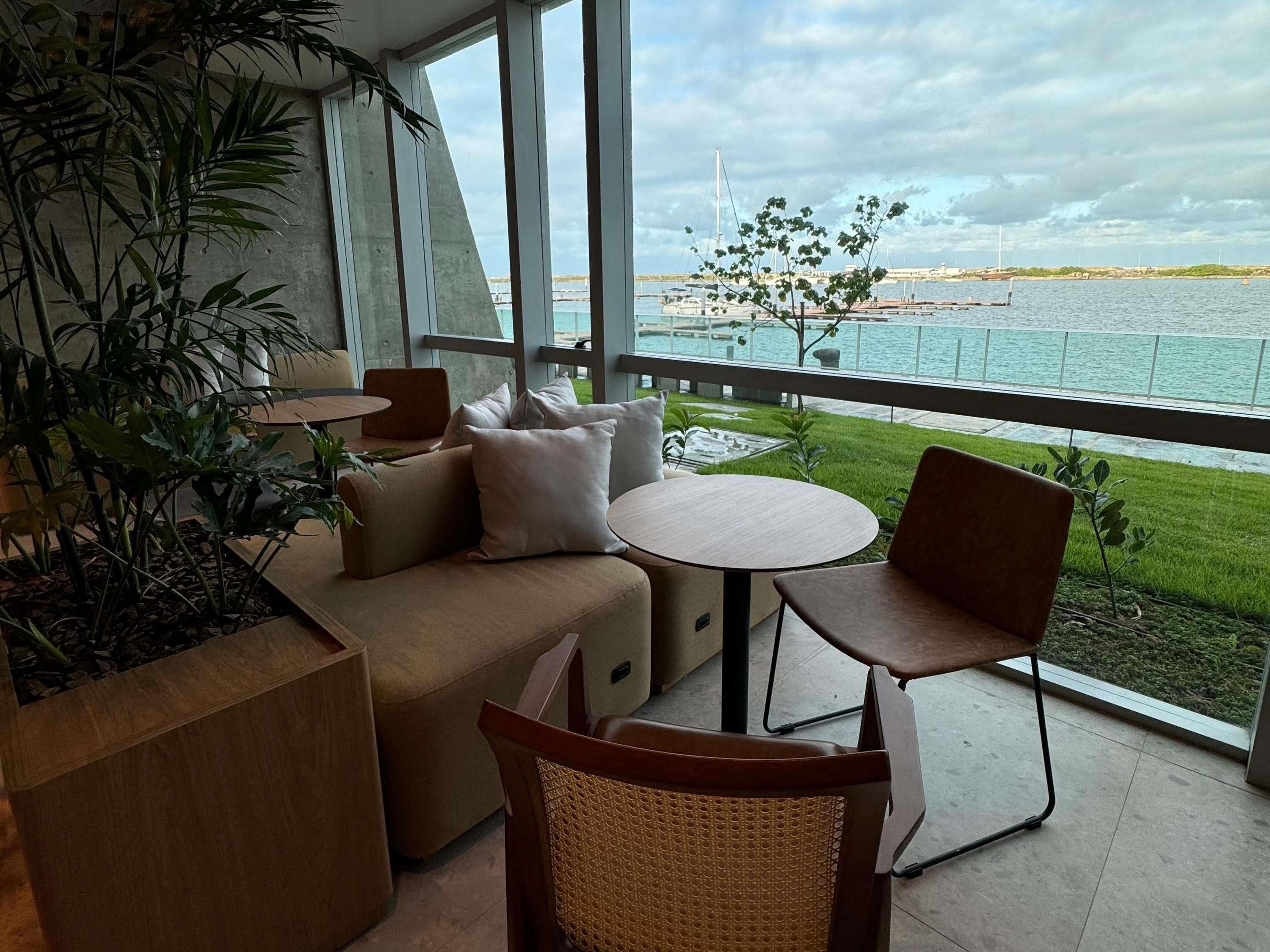 Un espacio al aire libre moderno con sofá, sillas y una pequeña mesa, con vista a un puerto deportivo con barcos y un puente.