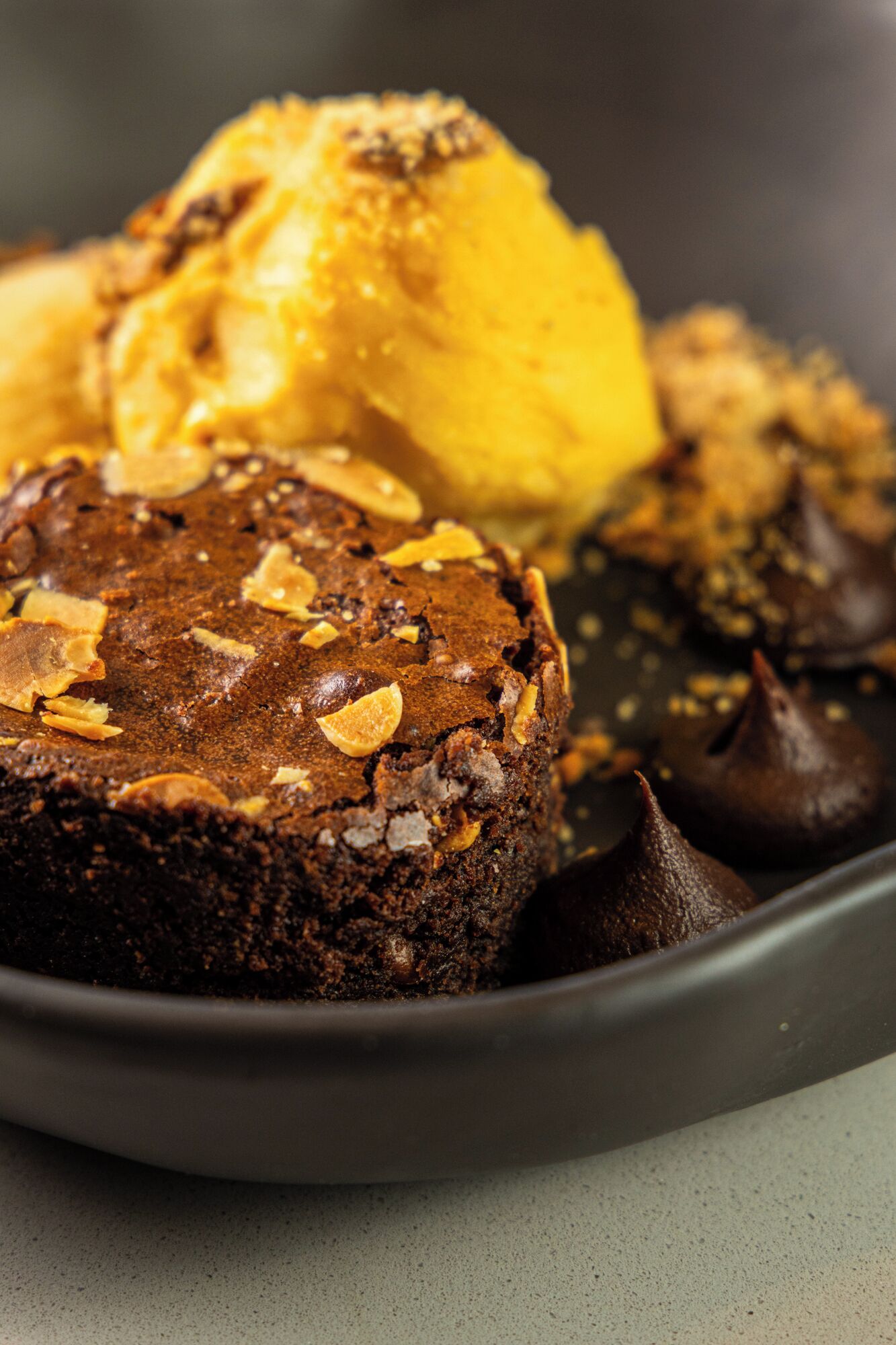 A dessert plate with a chocolate cake topped with almonds, a scoop of vanilla ice cream, and chocolate kisses.