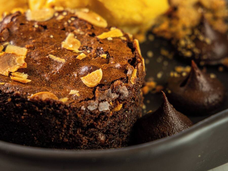 A dessert plate with a chocolate cake topped with almonds, a scoop of vanilla ice cream, and chocolate kisses.