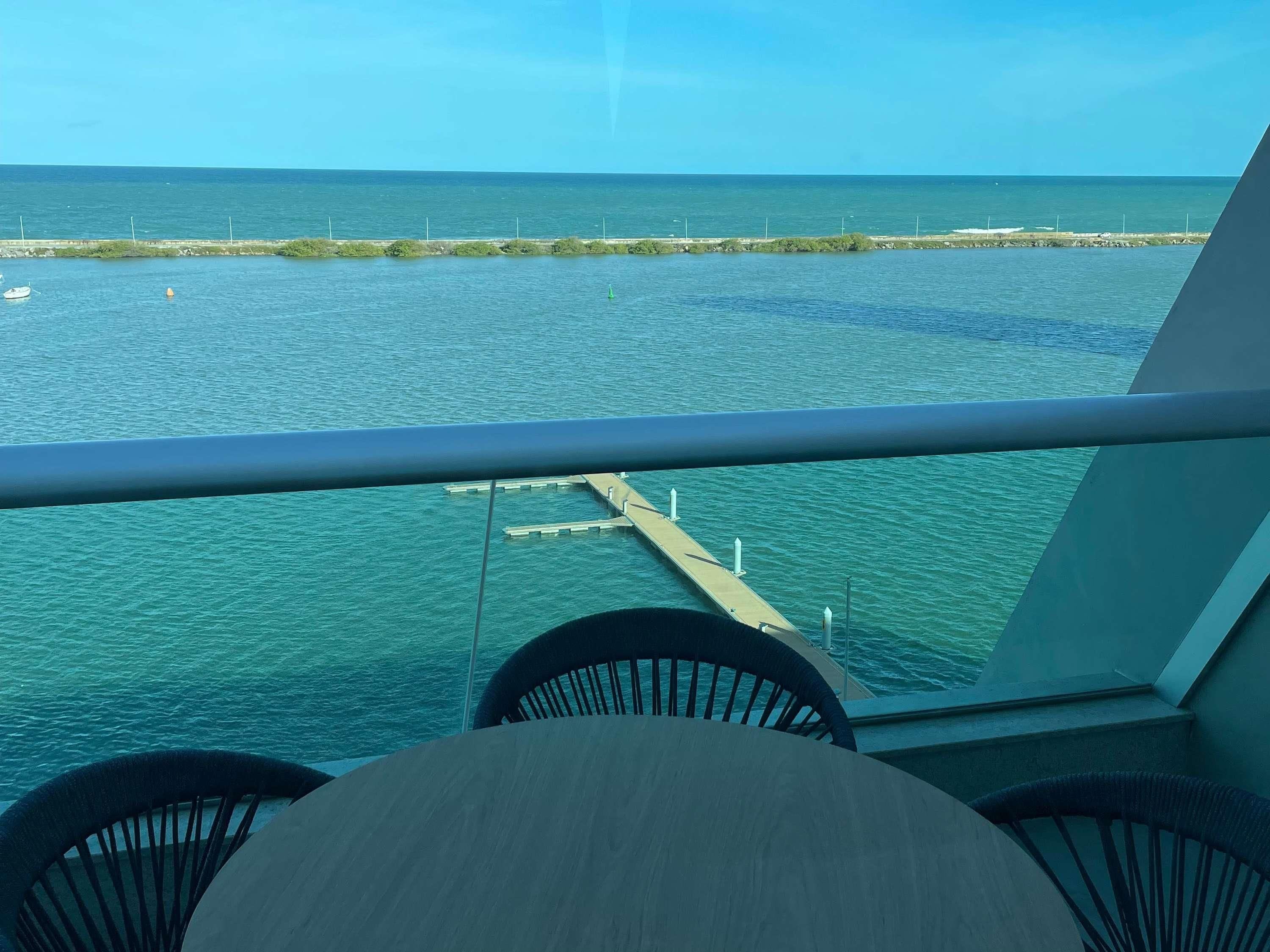 A balcony with a view of the sea, a pier, and a small boat.