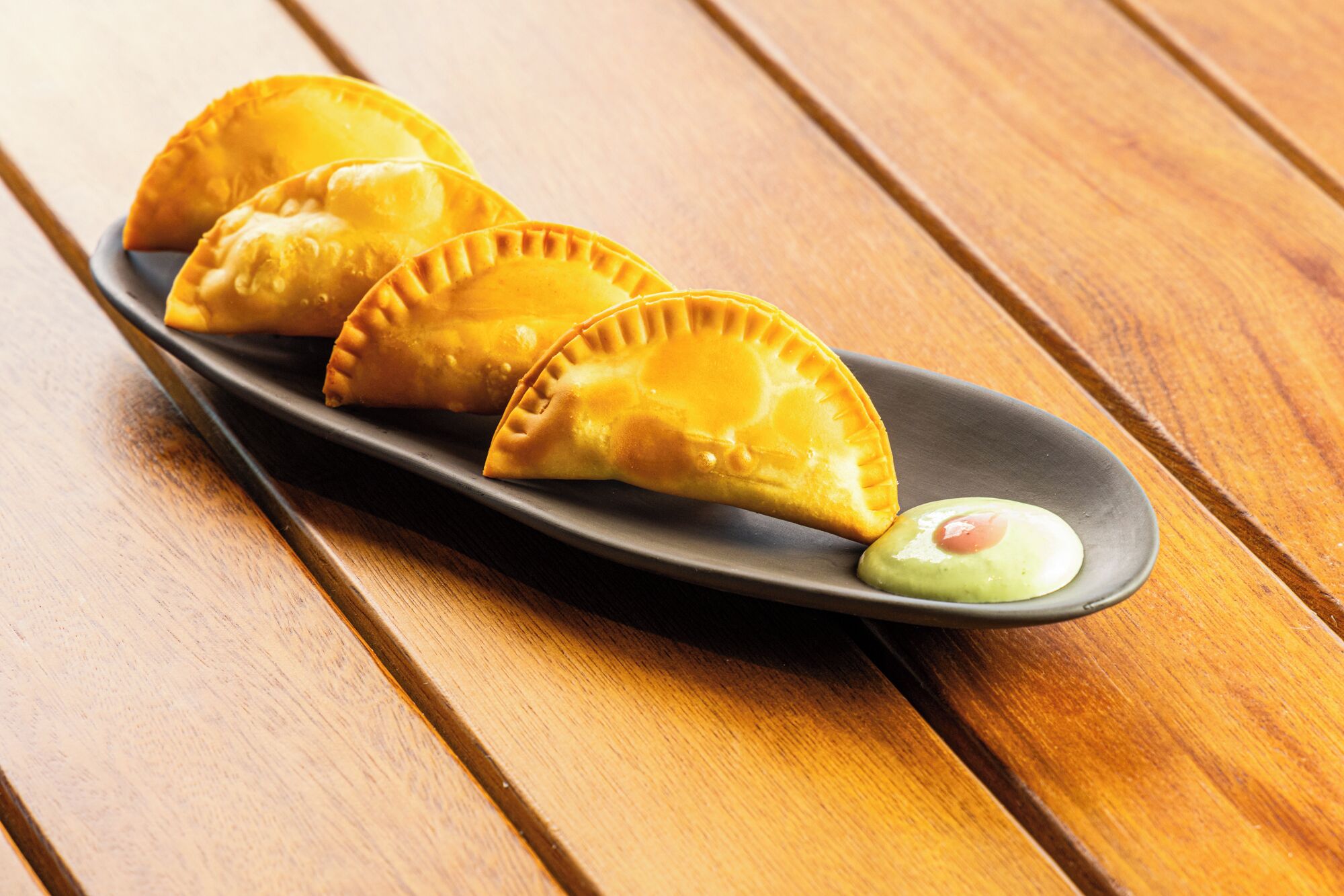 A plate with three golden-brown pastries on a dark plate, placed on a wooden table.