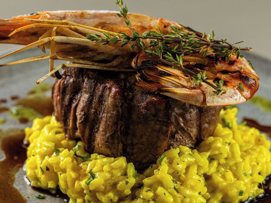 Plato con camarón sobre un filete, acompañado de risotto amarillo.
