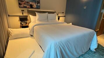 Quarto de hotel com uma cama grande, mesa de cabeceira com abajur, telefone e um quadro na parede.