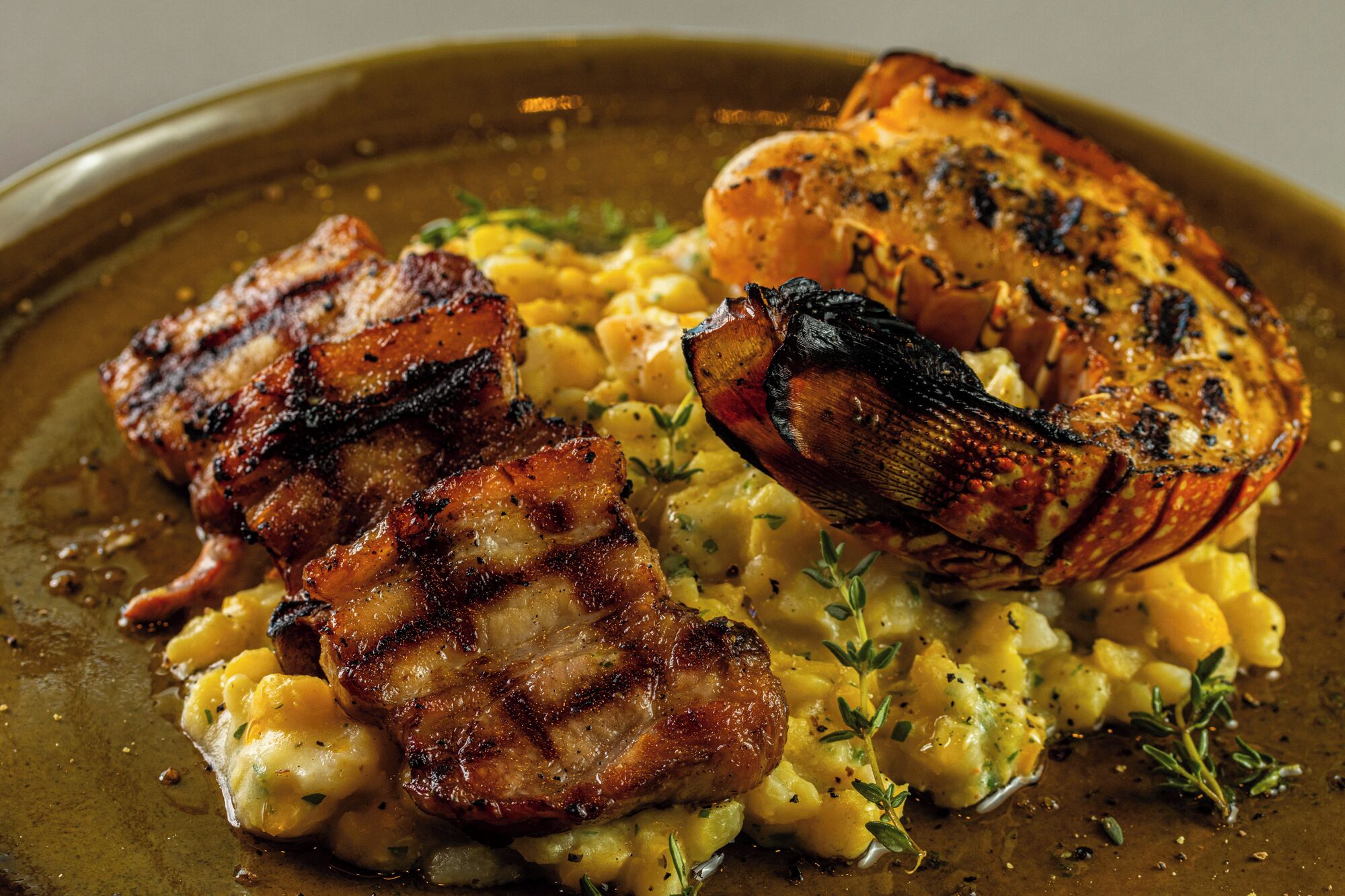 A plate with grilled meat, potatoes, and a scallop.