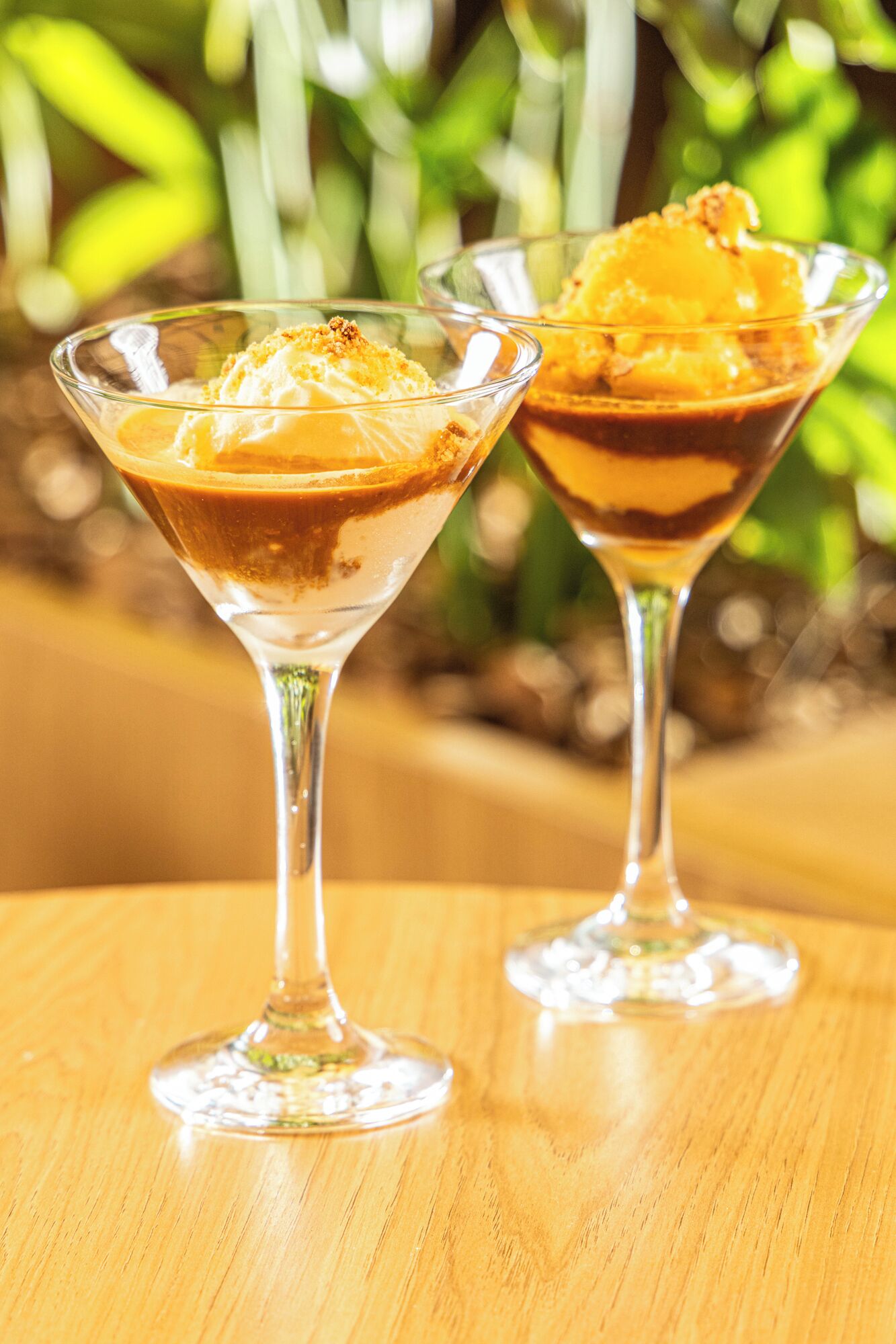Deux verres à dessert sur une table en bois, avec un arrière-plan flou de couleur verte.