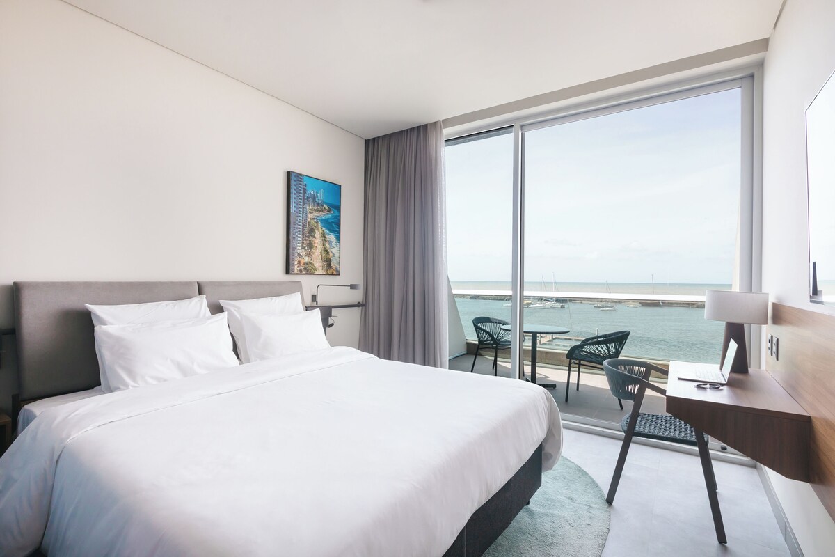 Una habitación de hotel con una cama grande, un escritorio con una computadora portátil y vistas al mar.