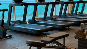 Un gimnasio con cintas de correr y máquinas de pesas, con amplias ventanas y vista al océano.