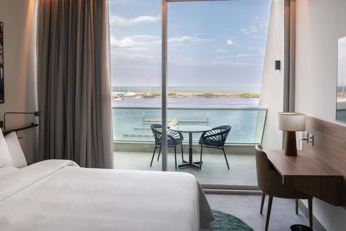 Ein Hotelzimmer mit Bett, Schreibtisch, Stuhl und Meerblick.