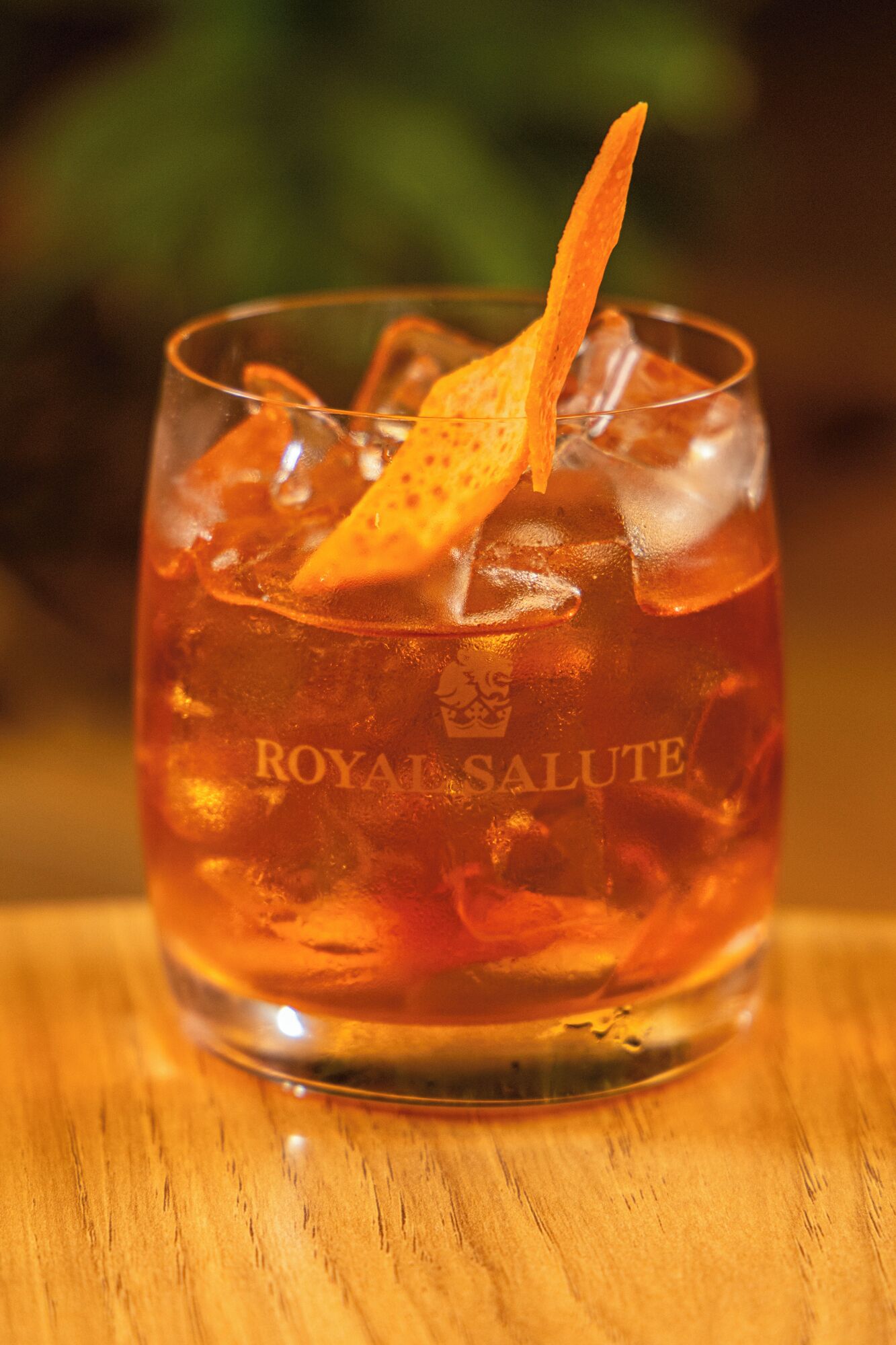 A glass of Royal Salute with ice cubes and a citrus garnish on a wooden surface.