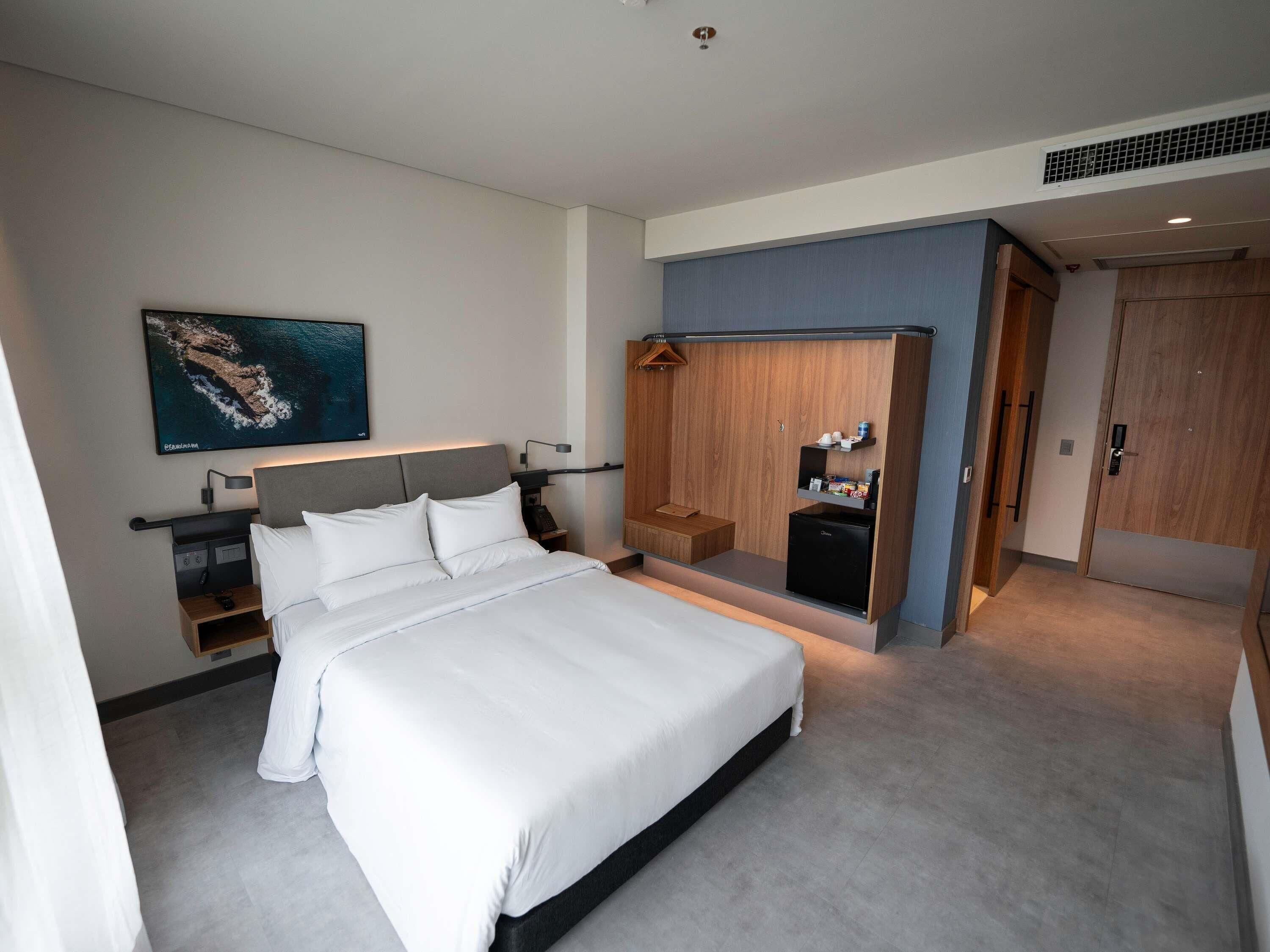 A modern hotel room with a large bed, a wardrobe with a mirror, a small desk, and a wall-mounted TV.