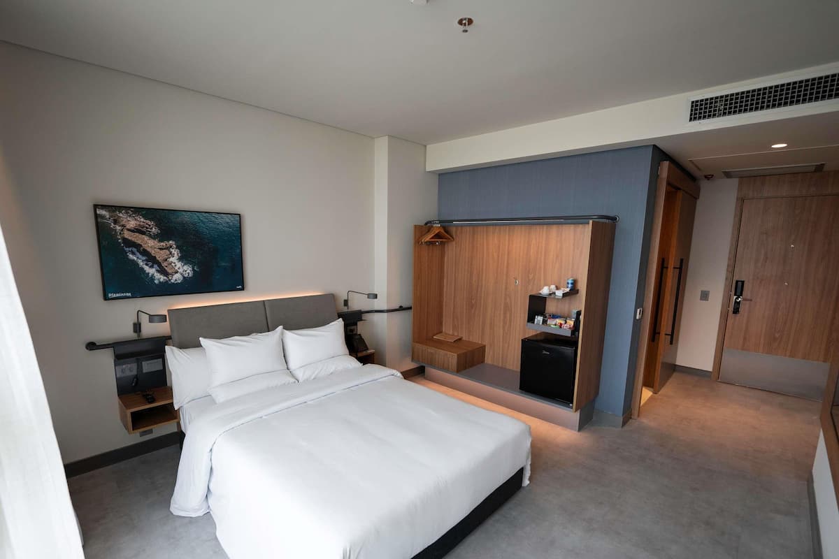 A modern hotel room with a large bed, a wardrobe with a mirror, a small desk, and a wall-mounted TV.