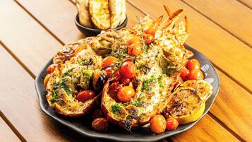Un plato de mariscos a la parrilla con tomates y hierbas, acompañado de pan sobre una mesa de madera.