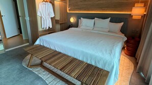 Una habitación de hotel moderna con una cama grande, un banco de madera y un vestidor con batas colgando.