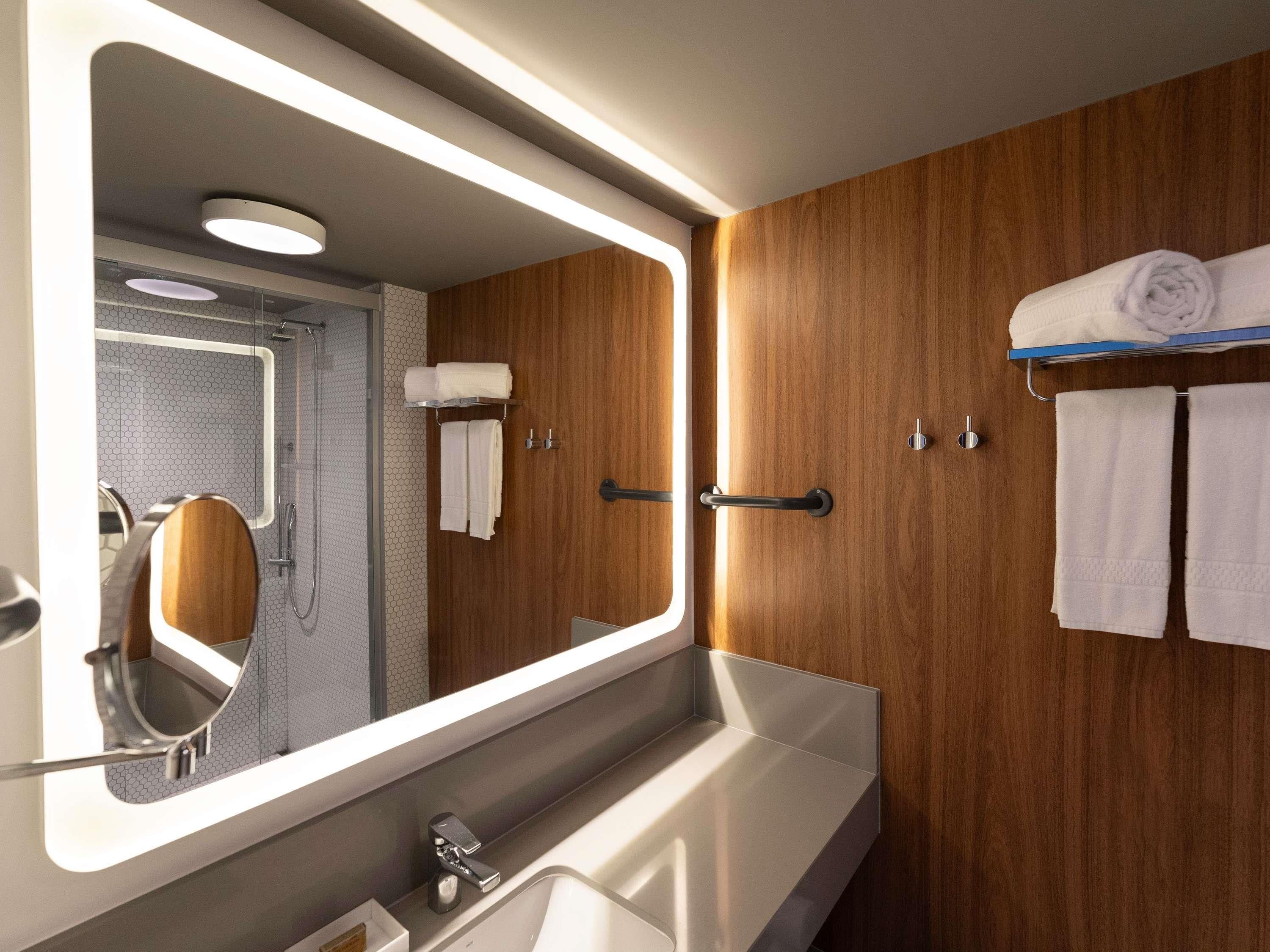 Un baño moderno con un espejo grande, paneles de madera, un lavamanos y un perchero para toallas.