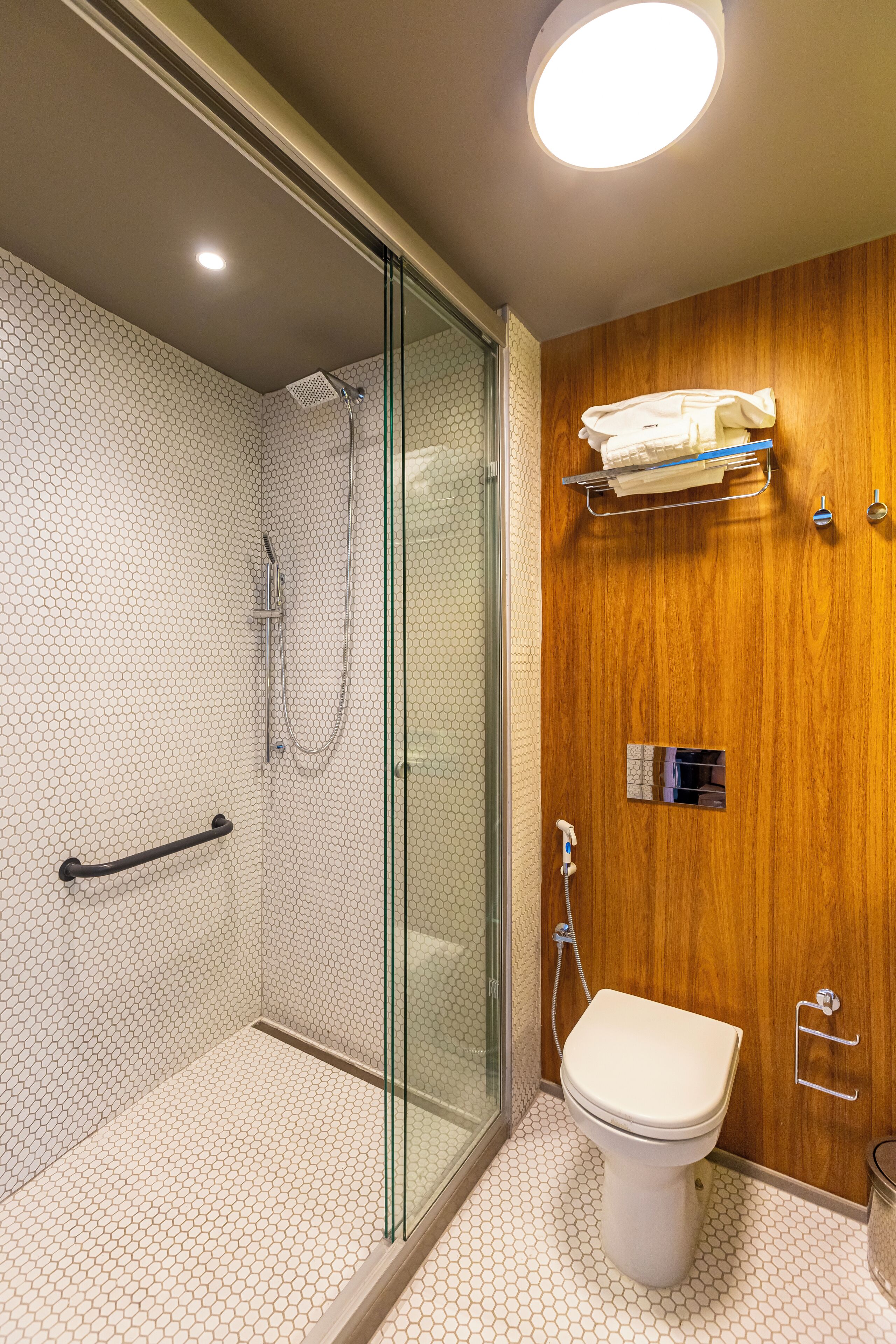 Een badkamer met een glazen douchecabine, een houten wastafelmeubel en een toilet.