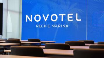 Un salón de conferencias con una pantalla grande que muestra 'NOVOTEL RECIFE MARINA'.