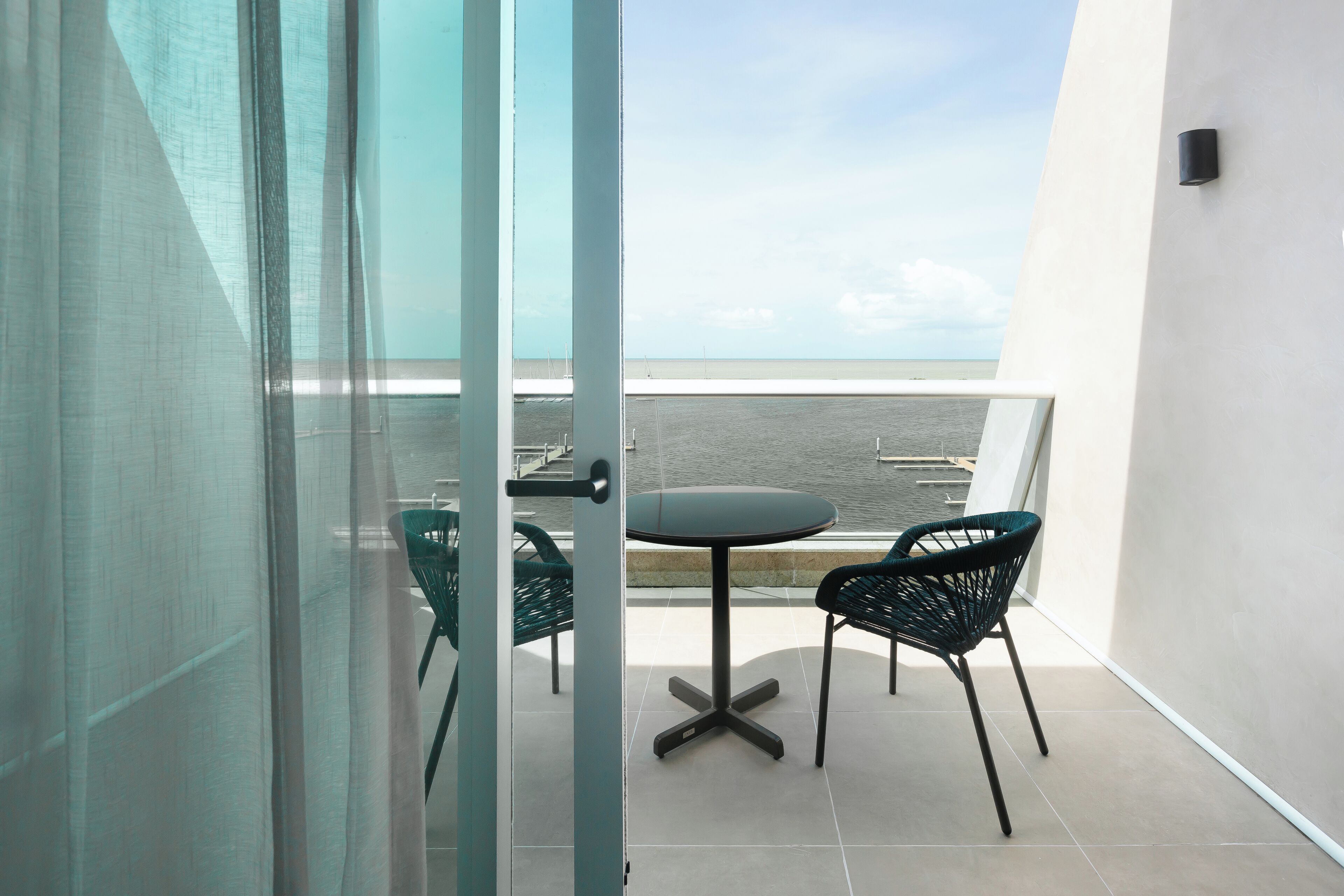 A balcony with a table and chairs, a view of the sea, and a glass door.