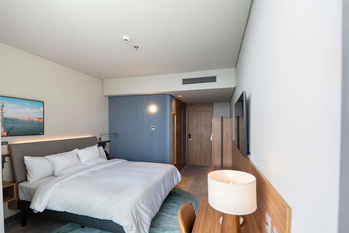 Ein modernes Hotelzimmer mit Bett, Nachttisch, Lampe und einem an der Wand befestigten Fernseher.